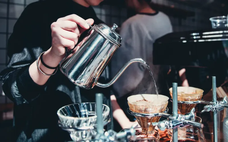 Barista pouring steamed milk into a cup of coffee behind a cafe counter