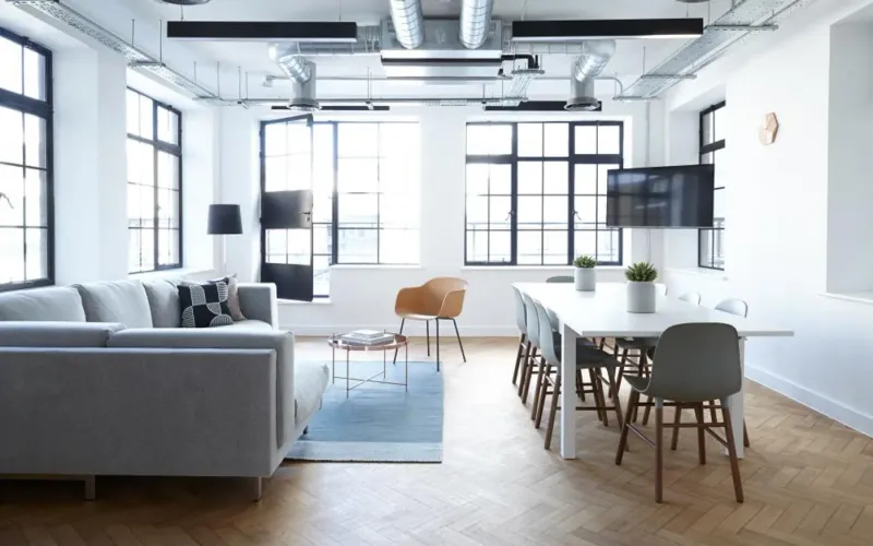 Bright open-plan living and dining room with a grey sofa and a long table